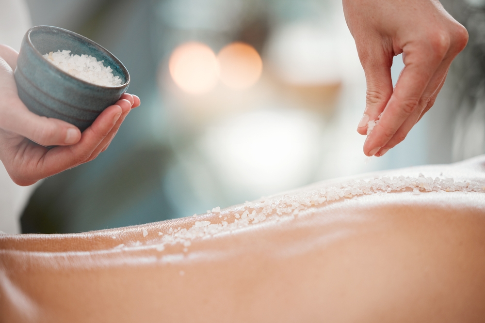 A salt body scrub being applied on a client’s back
