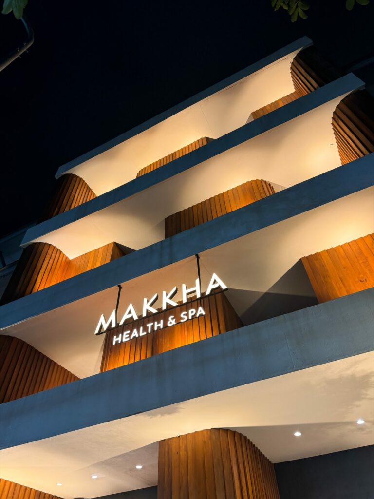 MAKKHA Health & Spa sign illuminated at night on a modern building facade featuring curved concrete balconies and warm wood paneling.