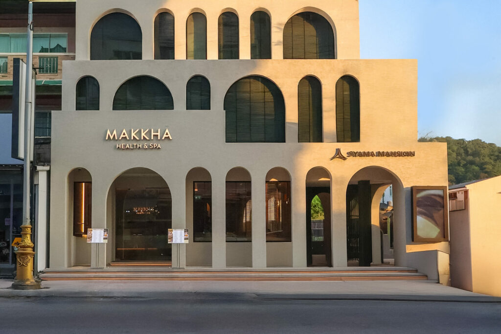 MAKKHA Health & Spa exterior in Phuket, showing the modern arched facade, gold signage, and the adjacent Syamamansion entrance.