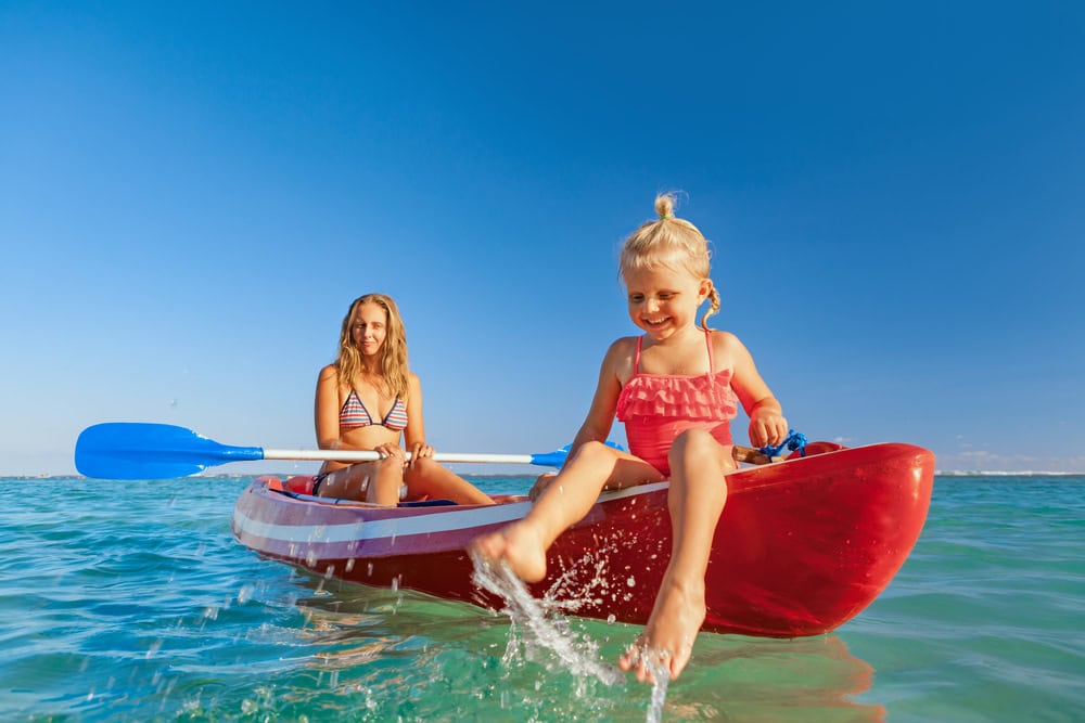 Two young girls enjoying a fun day kayaking on clear blue waters under a bright sunny sky in Chiangmai, Thailand.
